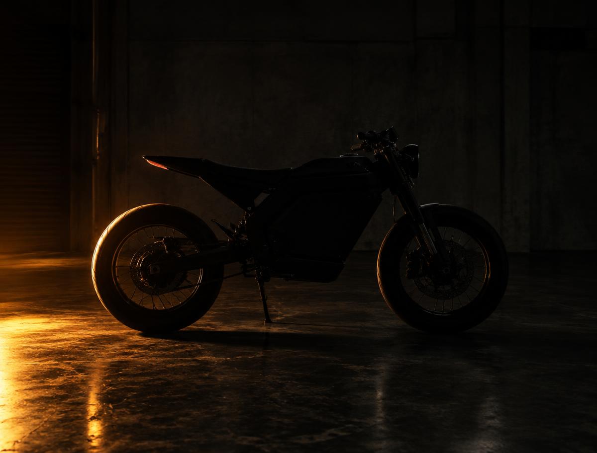 Blacked out electric moto lit by a single amber light in a garage